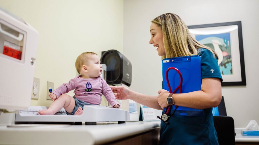 Doctor smiling at a baby that's sitting on a scale smiling back
